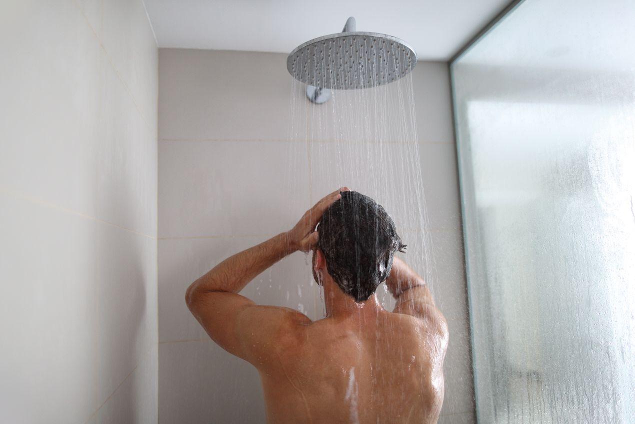 Duschrückwand Aluverbund hinter Mann unter Regendusche in minimalistischem Badezimmerdesign